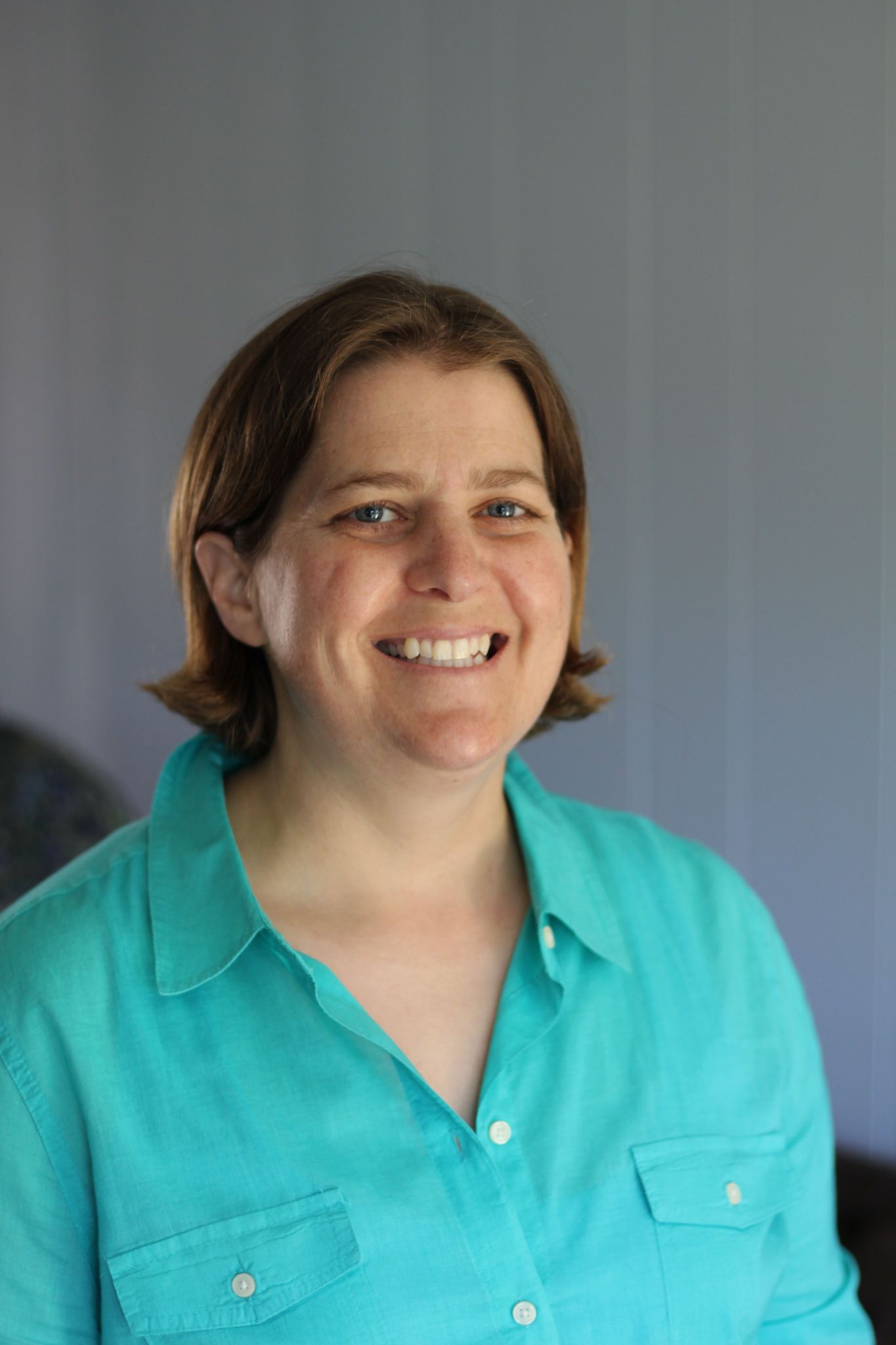 Image of Amie Lowery-Luyties, owner of Long Beach Therapy, wearing a light green long button-up shirt, smiling against a blurry grayish background.